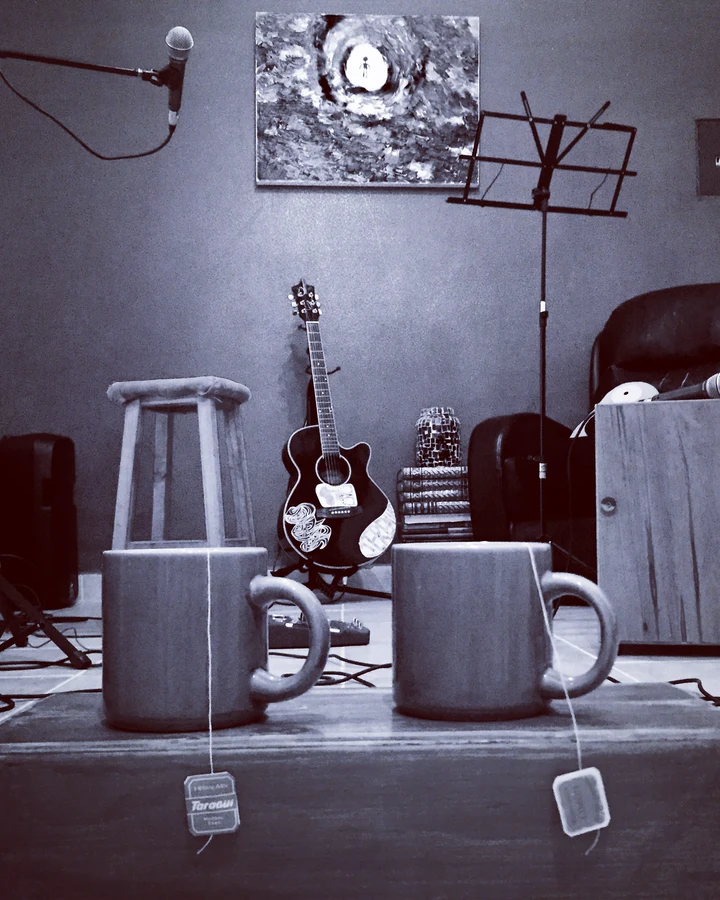 Estudio de música en blanco y negro: dos tazas con té sobre un cajón, un taburete, una guitarra y un atril.