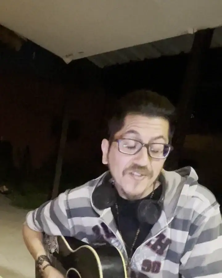 Jere Masih canta con la guitarra de noche, con auriculares al cuello y una laptop sobre una mesa verde.